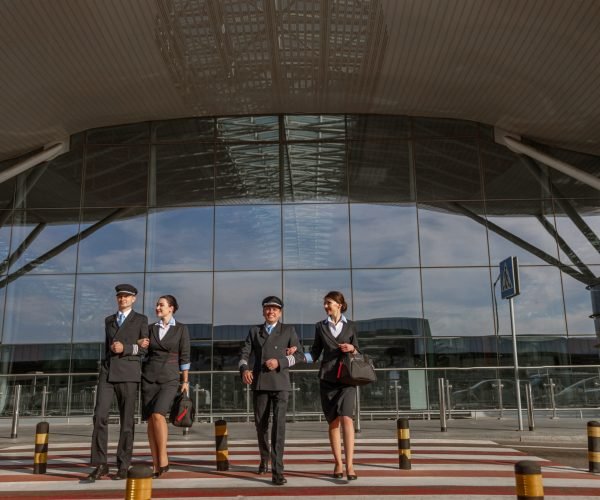 Full-length photo of happy flight team crossing the road outdoor with airport terminal on the background